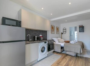Een compacte hotelkamer met kitchenette, wasmachine, een bed met uitzicht en een klein tafeltje.