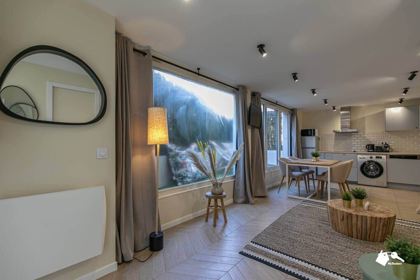 A modern apartment with a dining area, kitchen, and large windows.