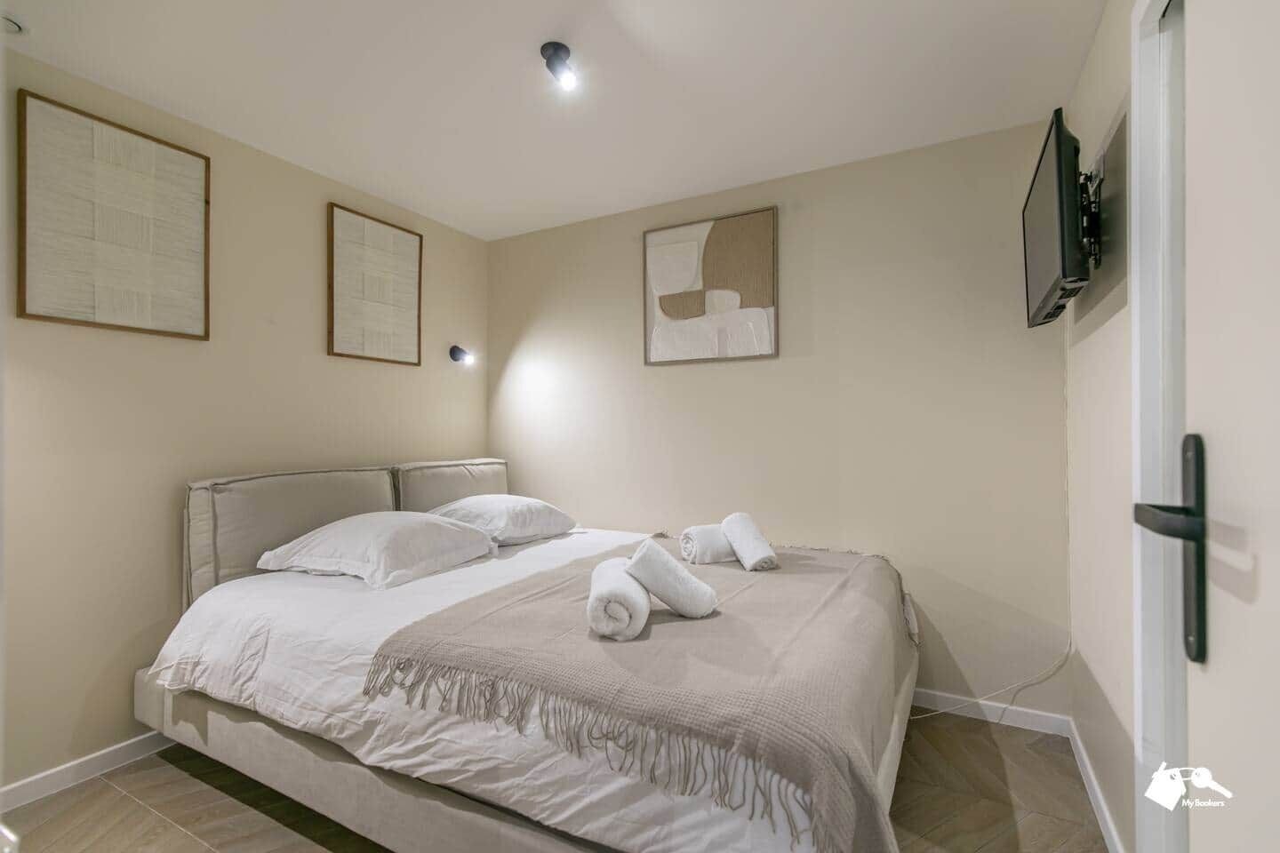 Une chambre à coucher avec un lit, des oreillers, une couverture et un téléviseur fixé au mur.