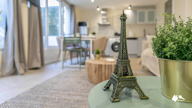 Un salon moderne avec une maquette de la tour Eiffel posée sur une table, un coin repas et une cuisine en arrière-plan.