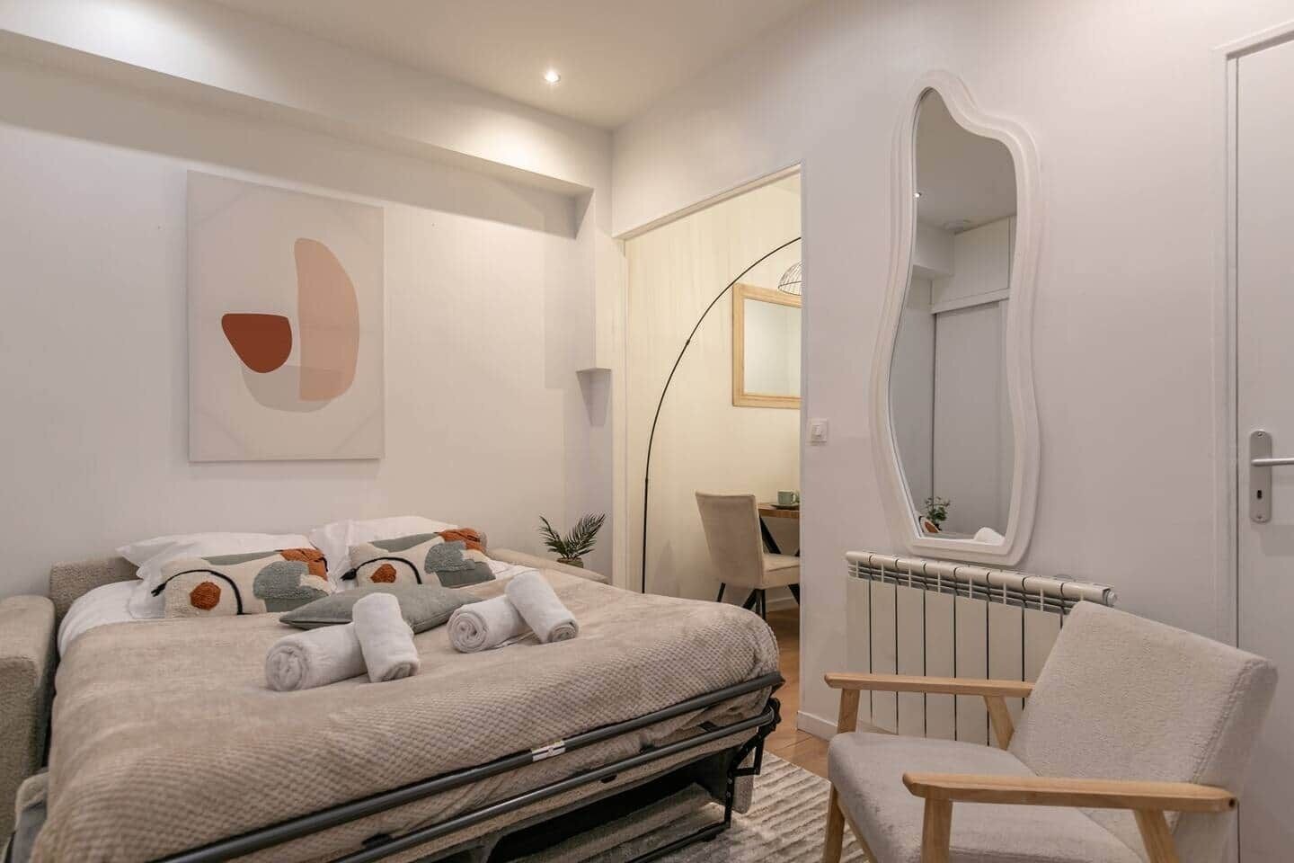 Un dormitori modern amb un llit, una cadira, un radiador i un mirall.