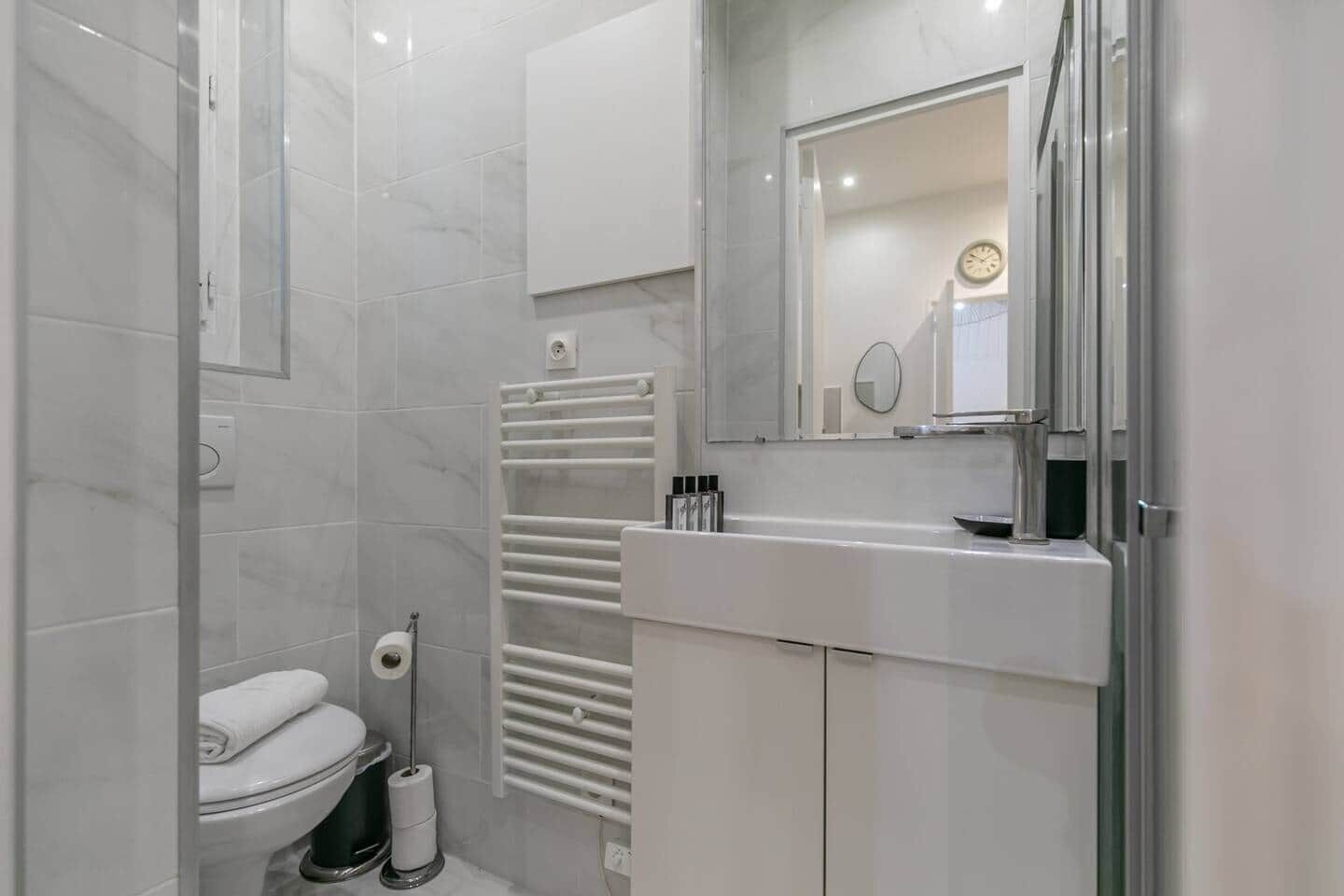 A modern bathroom with a toilet, a towel rack, a mirror, and a shower area.