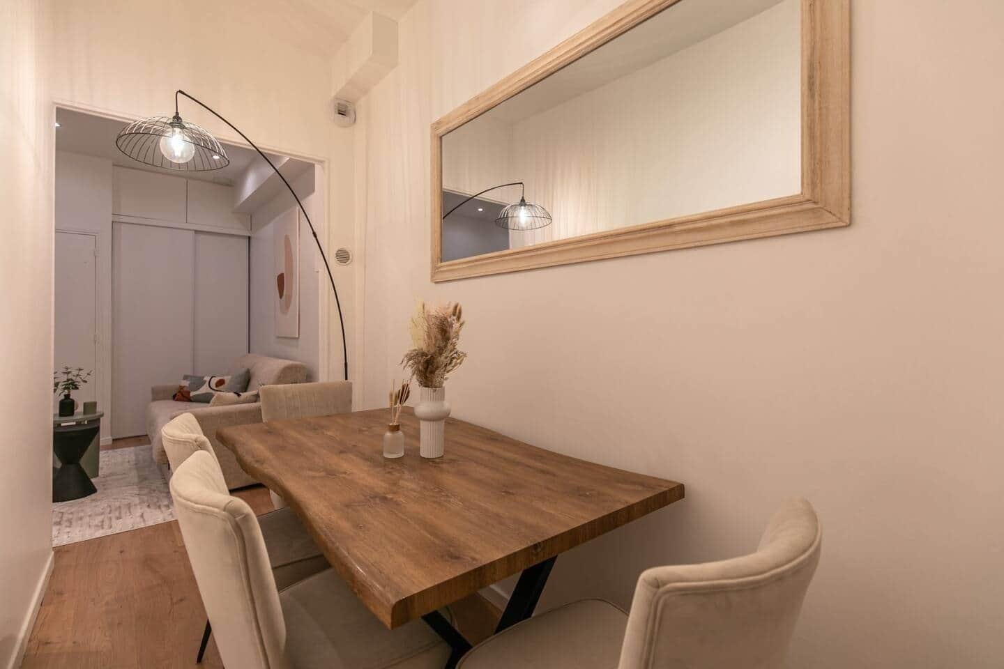 A dining area with a wooden table, white chairs, and a vase with dried plants.