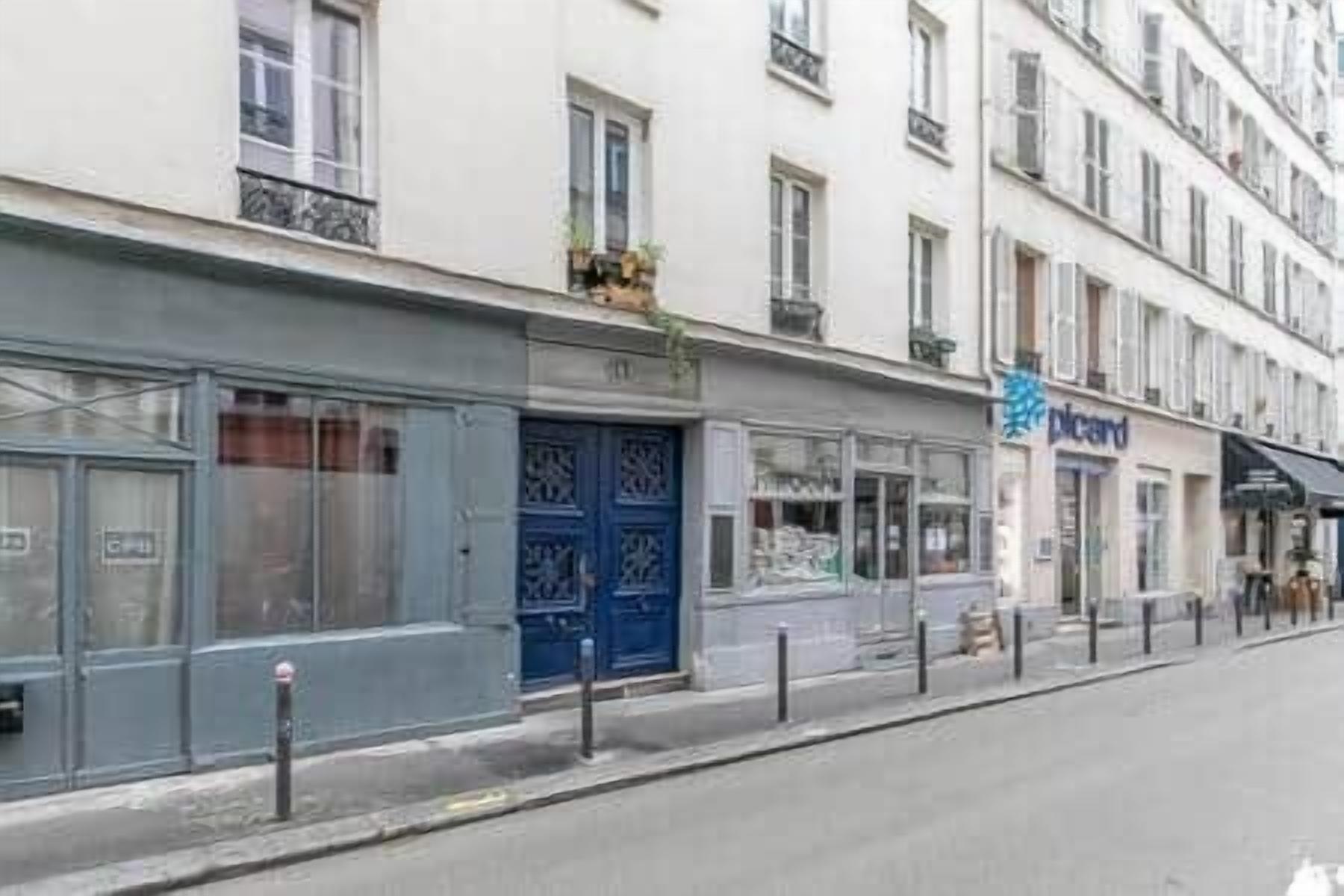 Una veduta di una strada con una fila di edifici, tra cui una porta blu e il cartello 'Plicard'.