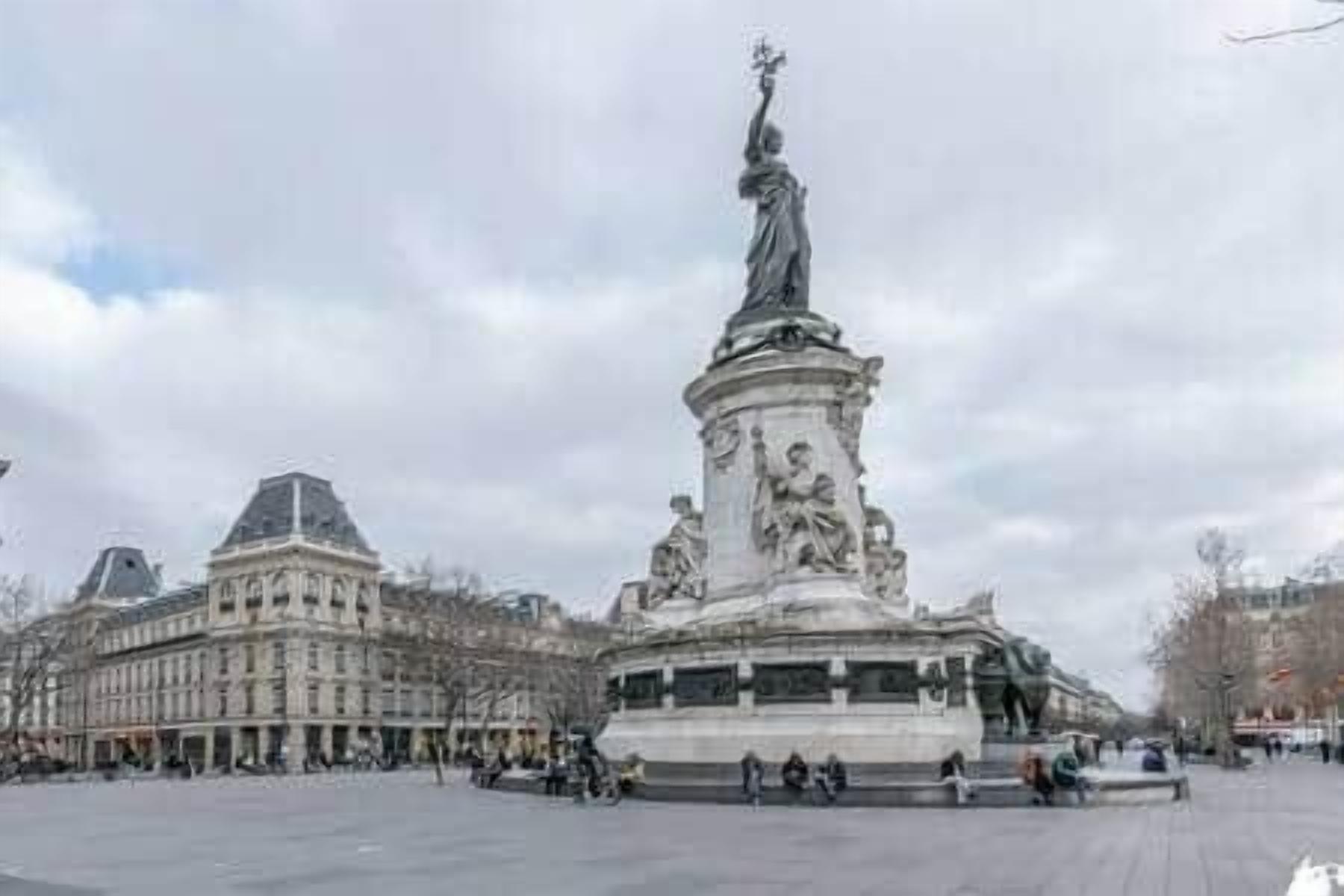 Une vaste place ouverte, avec un monument central sur lequel se trouve une statue d’une femme tenant une torche.
