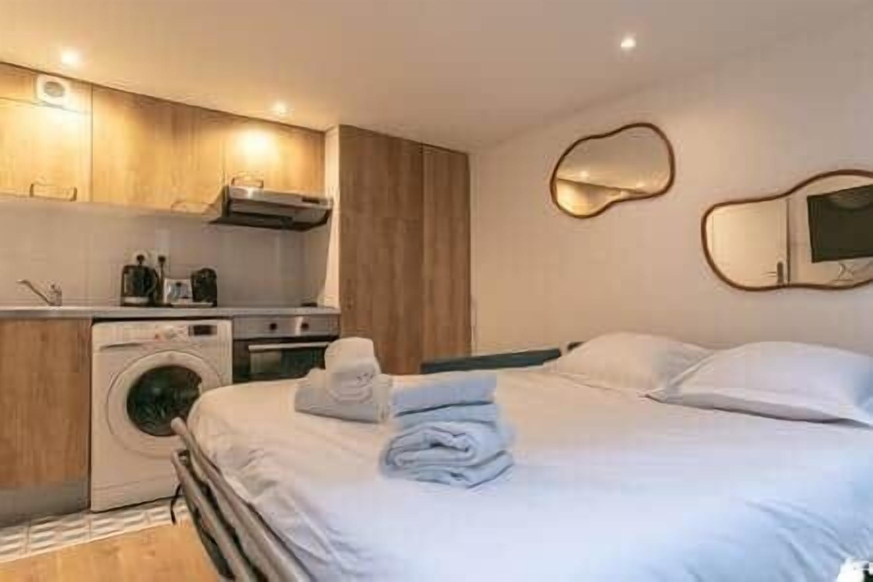 A modern hotel room with a neatly made bed, a washing machine, and a compact kitchenette.