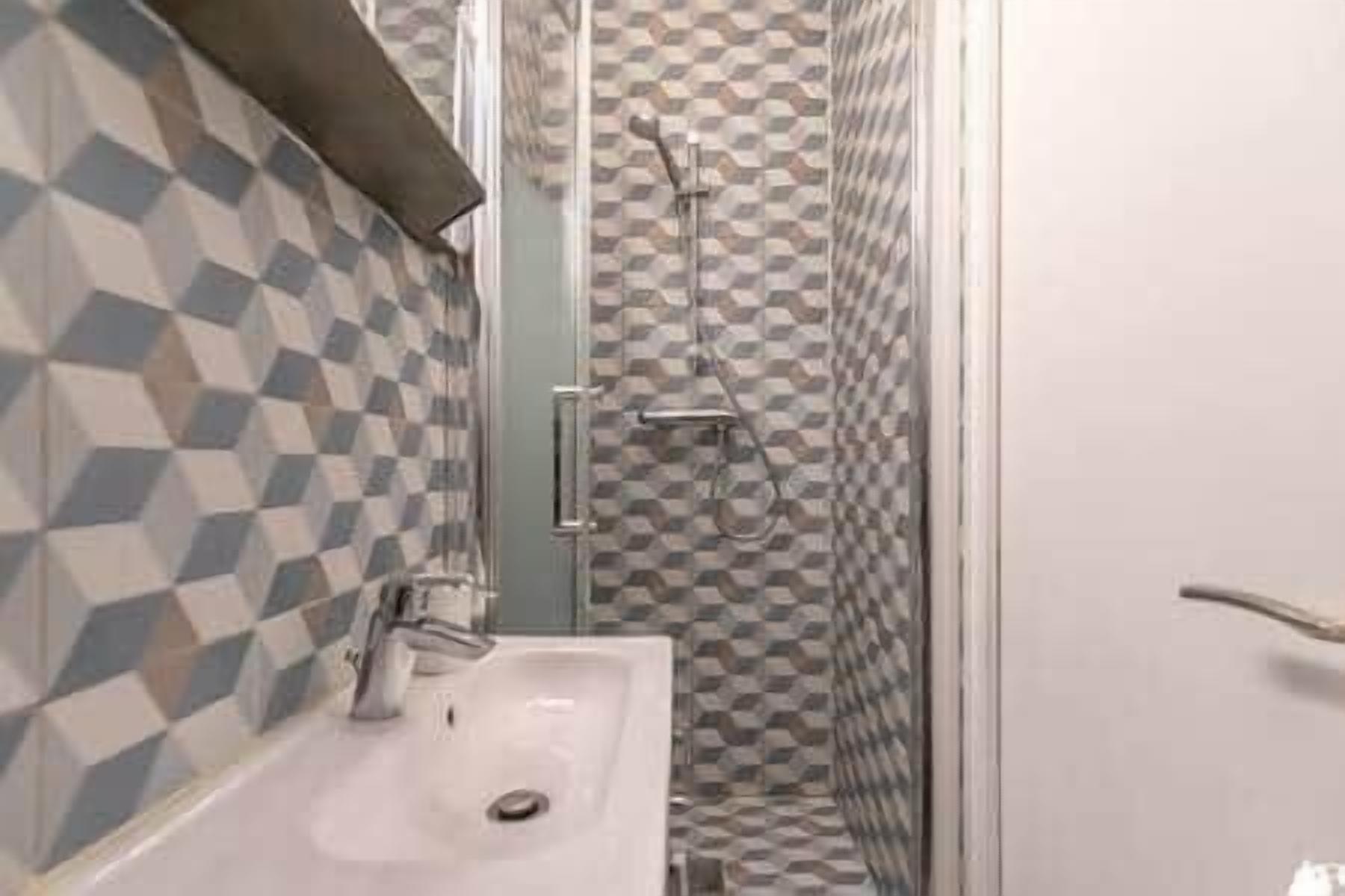 Een badkamer met een betegelde muur in een ruitpatroon, een witte wastafel en een douche met een glazen deur.