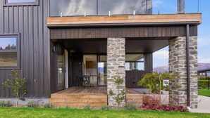 A modern building with a wooden deck, stone pillars, and a glass door leading to an interior space. - Kirimoko Heights (Wānaka)