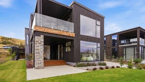 A modern two-story house with a stone facade, large windows, and a well-maintained lawn. - Kirimoko Heights (Wānaka)