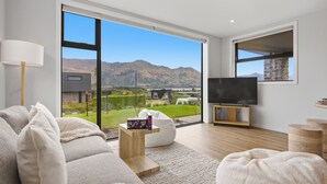A modern living room with a large window, a flat-screen TV, and a sofa. - Kirimoko Heights (Wānaka)