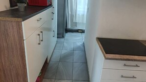 A narrow kitchen with white cabinets, a wooden countertop, and a tiled floor. - Lovely Room 15 min to Center via U3 Enkplatz Metro (Vienna)