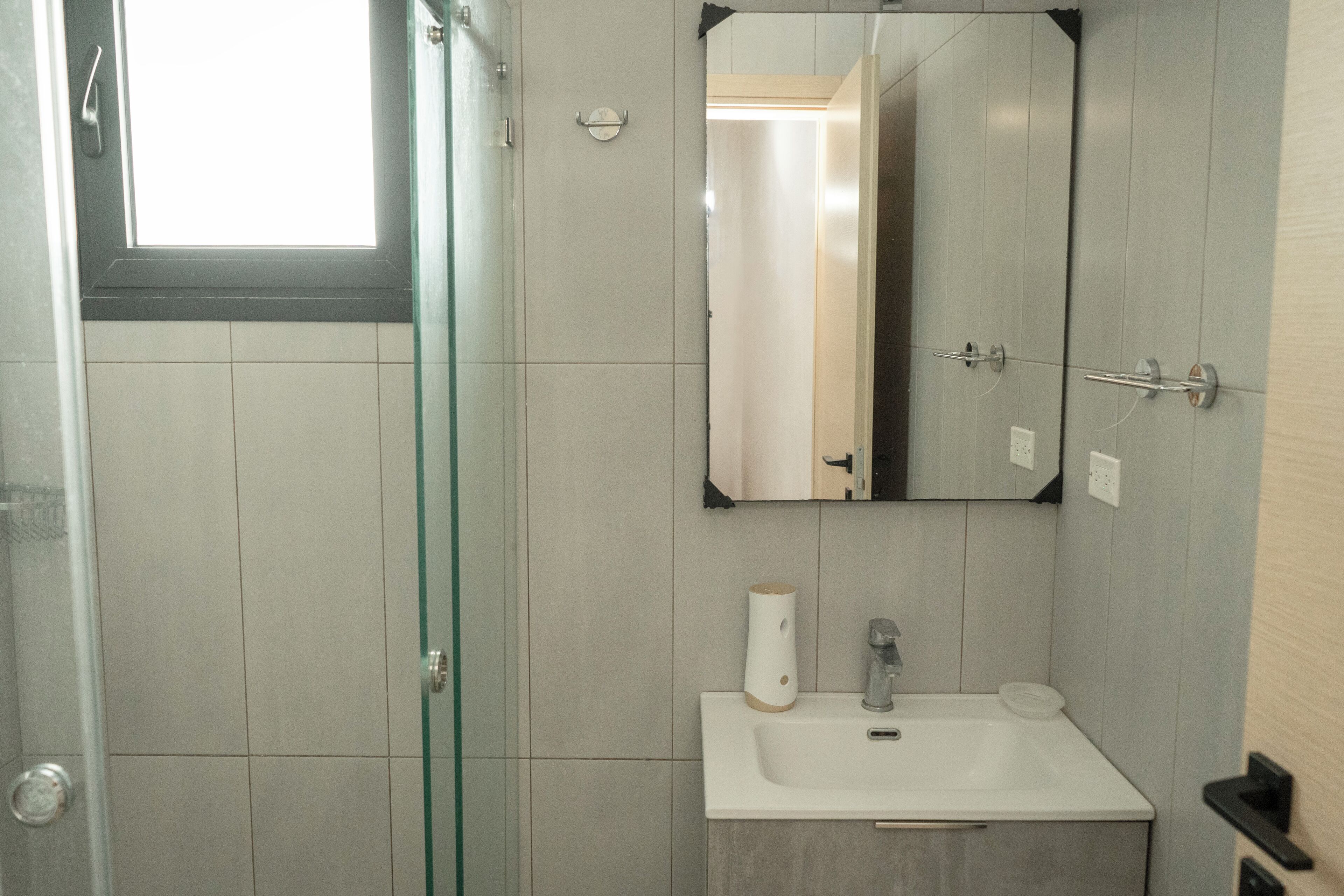 A bathroom with a glass shower door, a white sink, a mirror, and a towel dispenser.