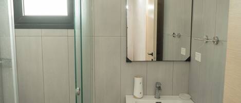 A bathroom with a glass shower door, a white sink, a mirror, and a towel dispenser.