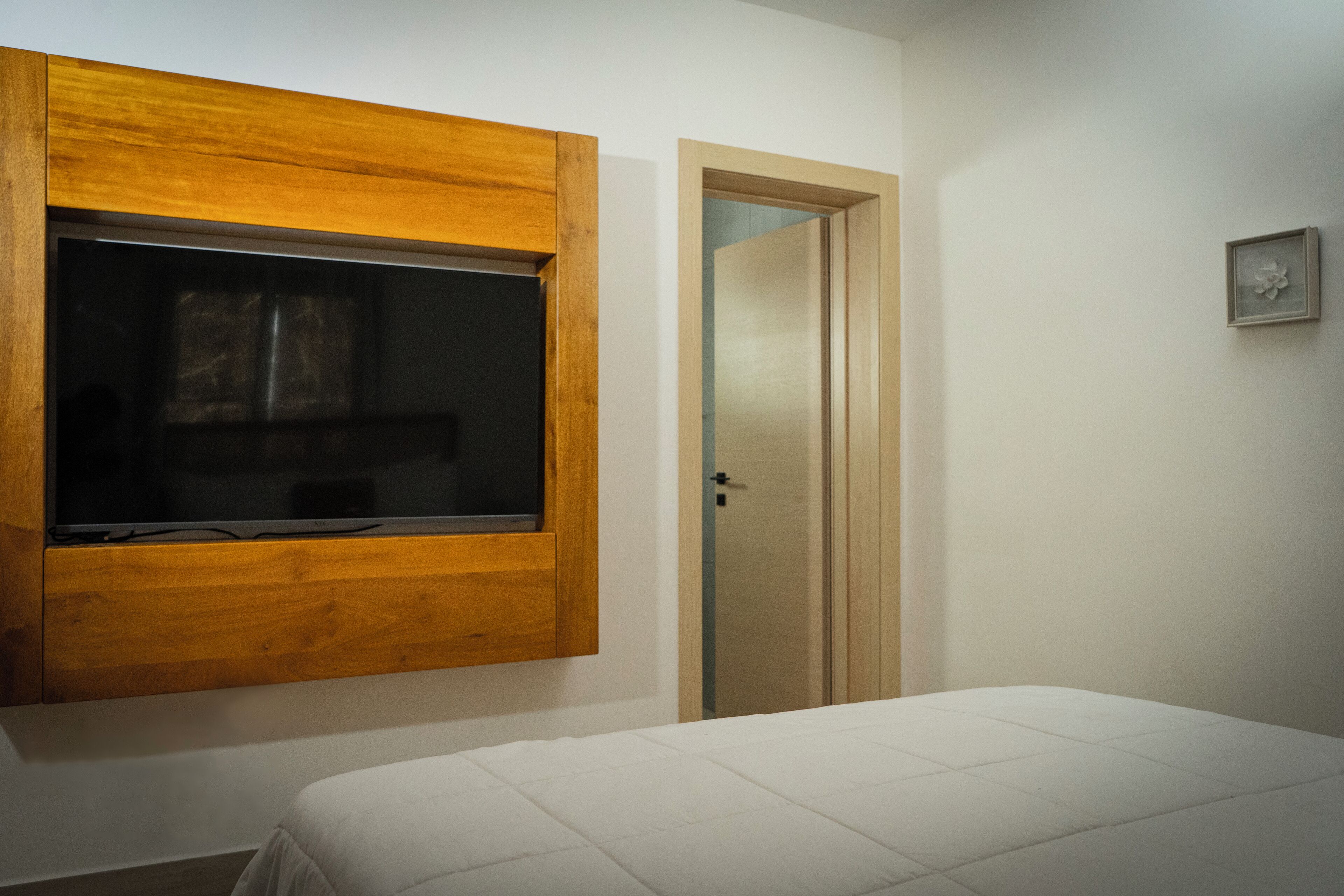 Ein Schlafzimmer mit einem Bett, einem Holzfenster, einer Tür und einer kleinen Wanddekoration.
