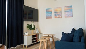 Un salon avec un téléviseur, trois tableaux, une plante, un canapé et une petite table.
