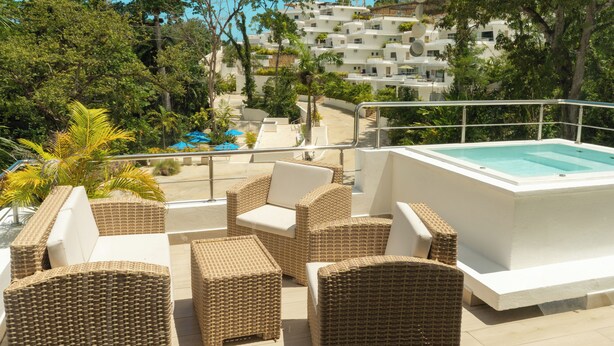 Une terrasse sur le toit, aménagée avec des meubles en osier, une piscine et une vue sur une colline parsemée de bâtiments blancs.
