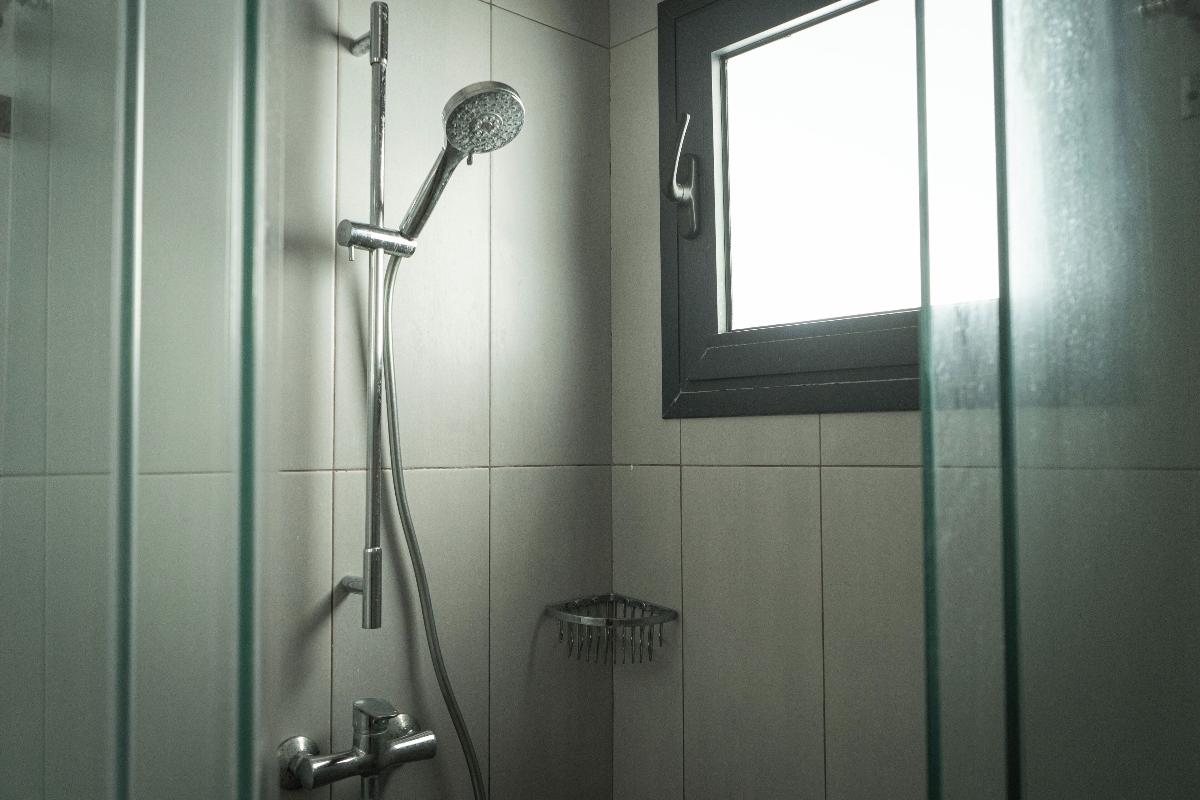 A shower with a handheld showerhead, a glass-enclosed shower area, and a window above the shower.
