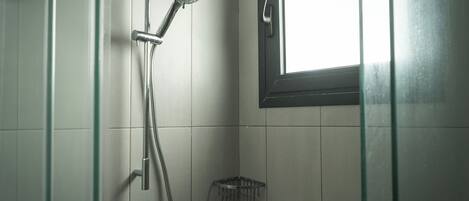 A shower with a handheld showerhead, a glass-enclosed shower area, and a window above the shower.