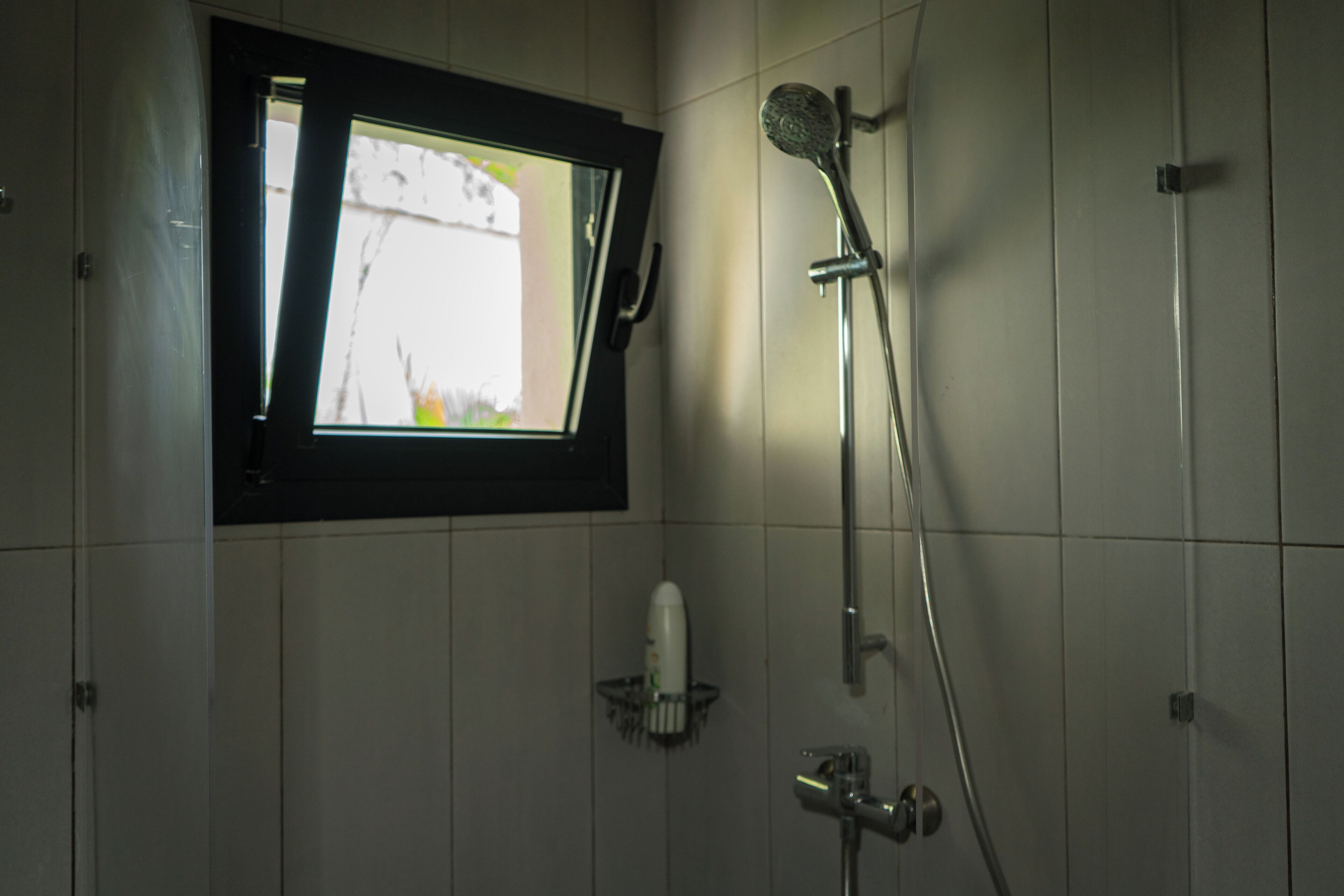 A bathroom with a window, a showerhead, and a soap dispenser.