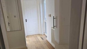 Un pasillo con suelo de madera, paredes blancas y una puerta que da a otra habitación.