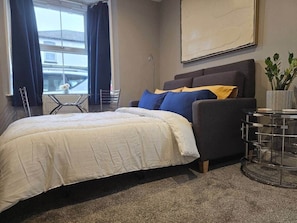 A bedroom with a bed, a sofa, a round glass coffee table, and a potted plant. - Stay Zen Apartments - Free Parking & Garden Woking (Woking)