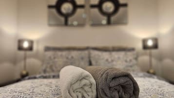 A neatly made bed with rolled towels, a patterned bedspread, and two wall-mounted lamps.