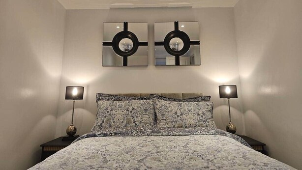 Un dormitorio con una cama, dos espejos en la pared y dos lámparas de noche.