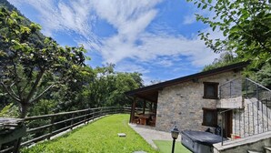 Une maison en pierre avec une terrasse en bois, un patio couvert et un escalier en pierre menant à un balcon.