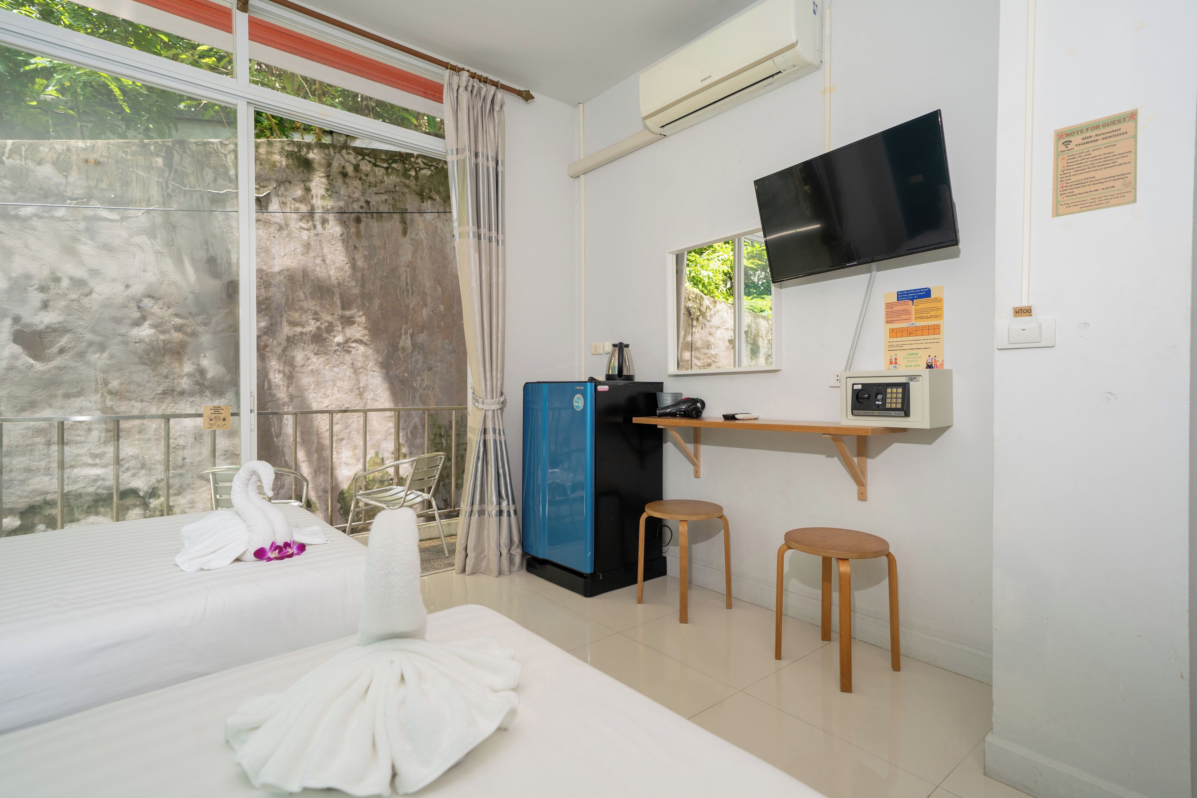 A hotel room with a bed, a desk with a computer, a TV, and a window with curtains.