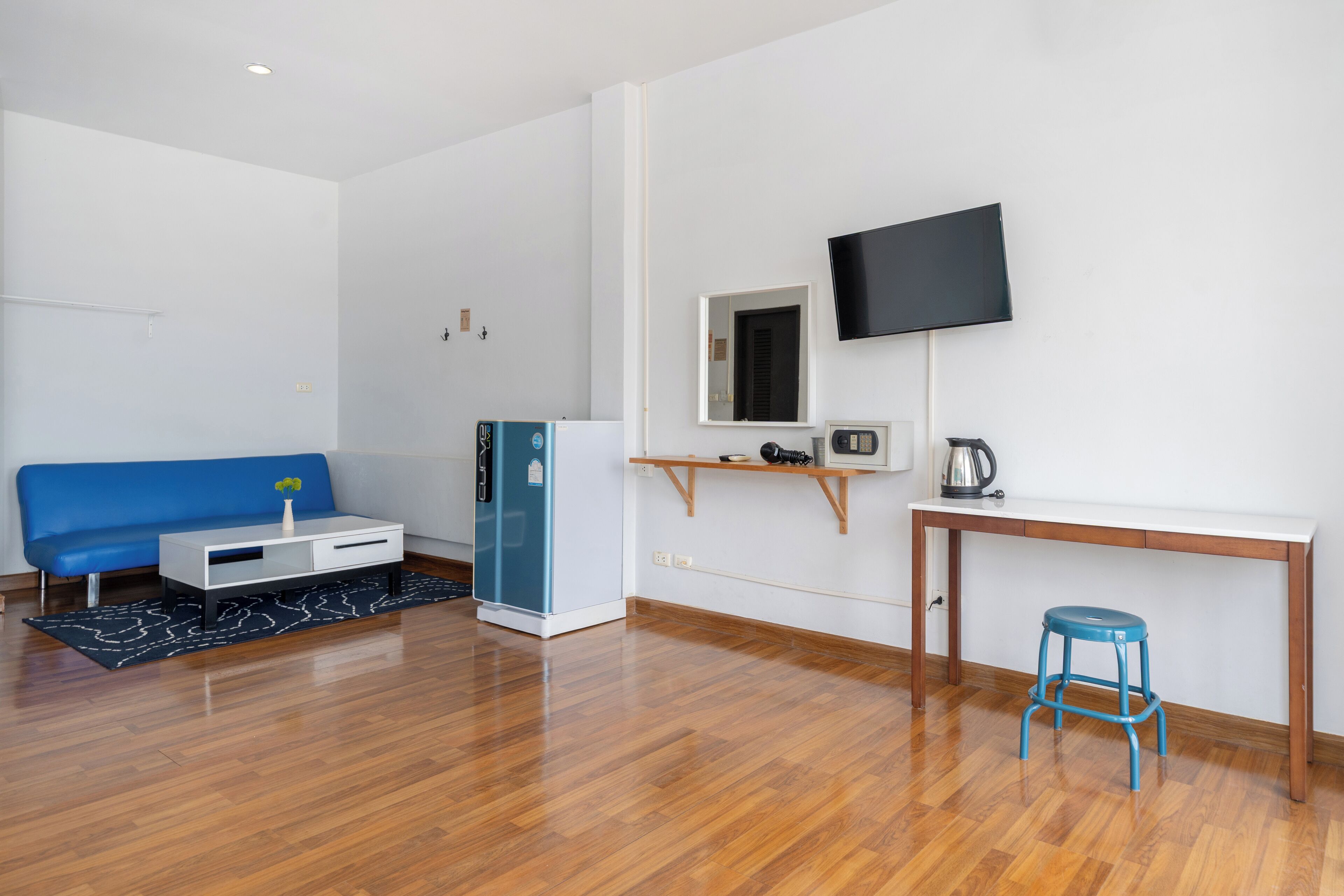 A modern room with a blue sofa, a white desk, a television, and a small stool.