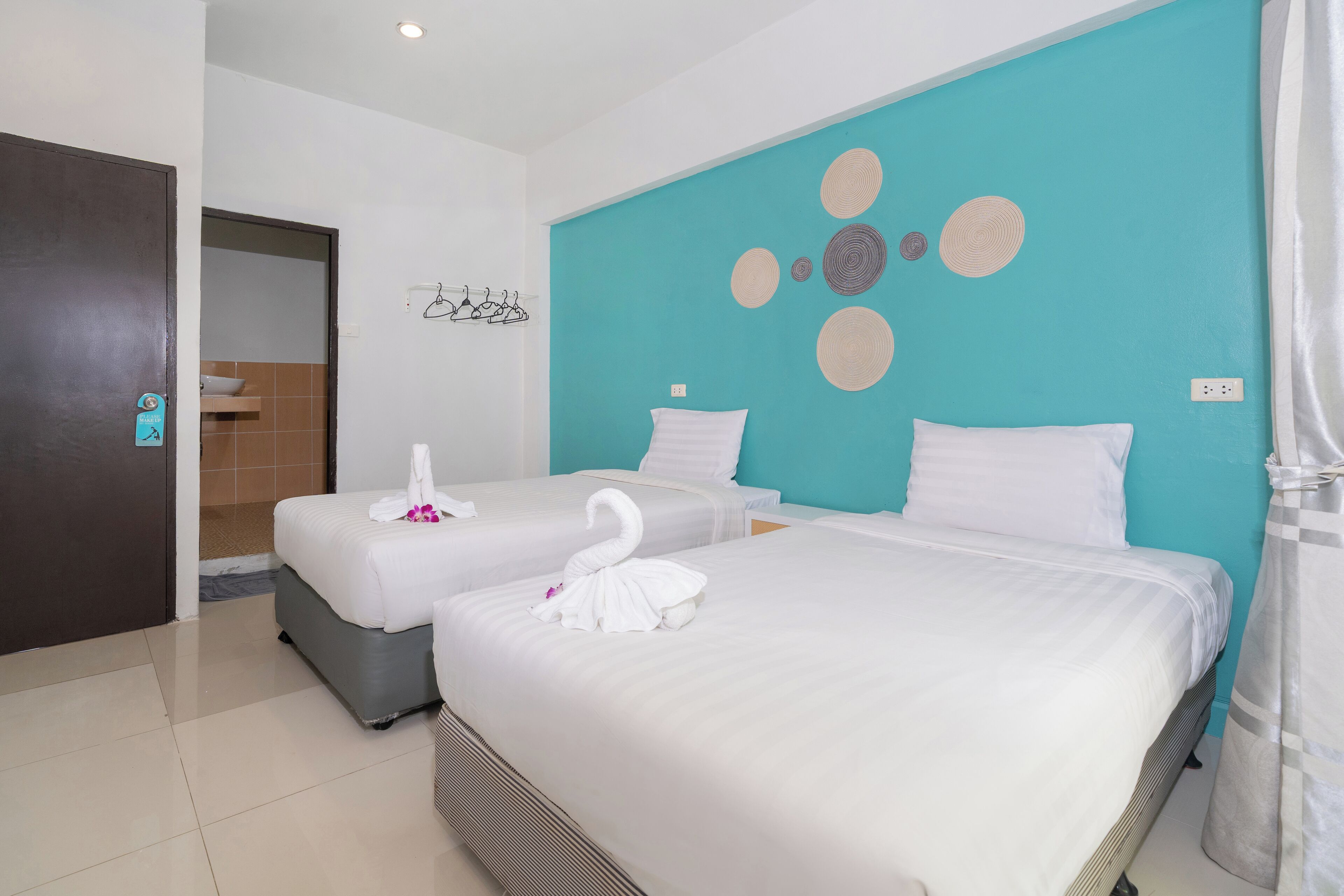 Ein Hotelzimmer mit zwei Betten, einer Wand in Türkis und einer Tür zum Badezimmer.