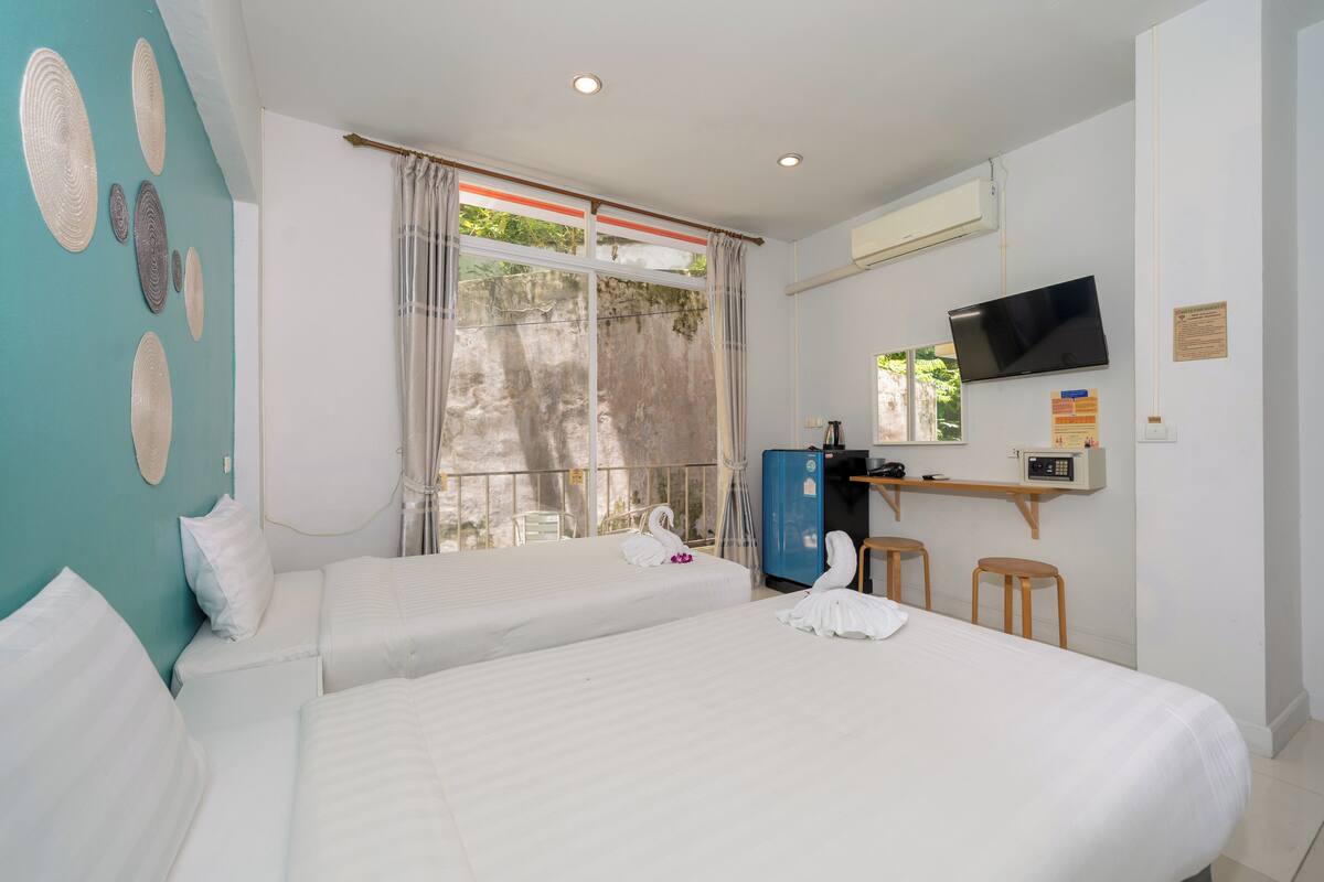 A hotel room with two beds, a TV, a desk with a computer, and a window with curtains.