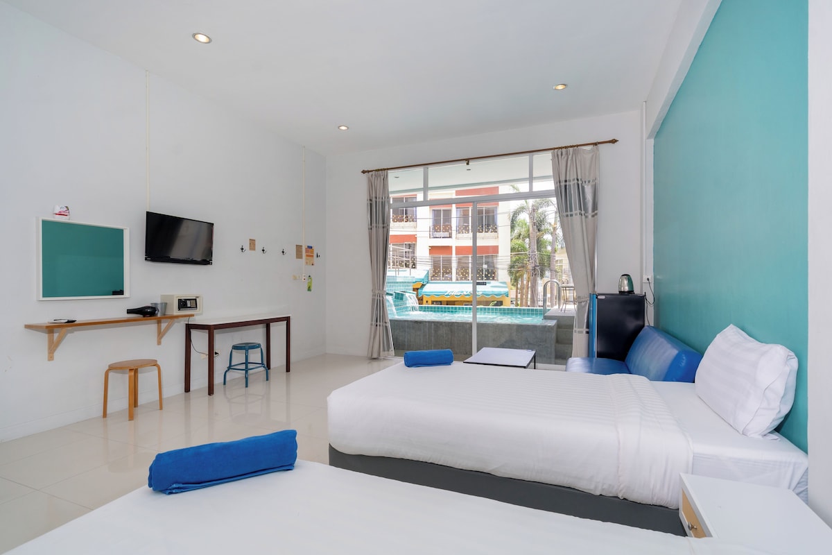 A hotel room with a bed, a desk, a TV, and a view of an outdoor swimming pool.