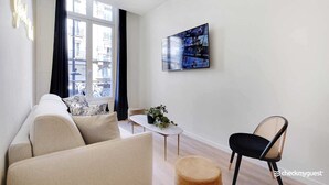 A modern living room with a sofa, a round table, a chair, and a TV mounted on the wall. - Charming 3-bedroom Flat - Le Marais (Paris)