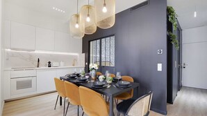 A modern kitchen with white cabinets, a black dining table set with yellow chairs, and a dark accent wall. - Charming 3-bedroom Flat - Le Marais (Paris)