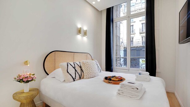 A hotel room with a bed, a bedside table with a vase of flowers, a tray of fruits, and towels. - Charming 3-bedroom Flat - Le Marais (Paris)