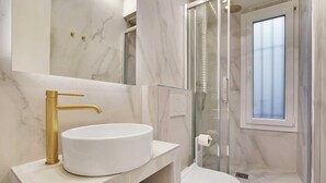 A modern bathroom with a marble vanity, a gold faucet, and a glass shower enclosure. - Charming 3-bedroom Flat - Le Marais (Paris)