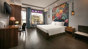 Ein Hotelzimmer mit einem großen Bett, einem Schreibtisch mit Lampe, einem Fernseher und einem farbenfrohen Blumenbild an der Wand.