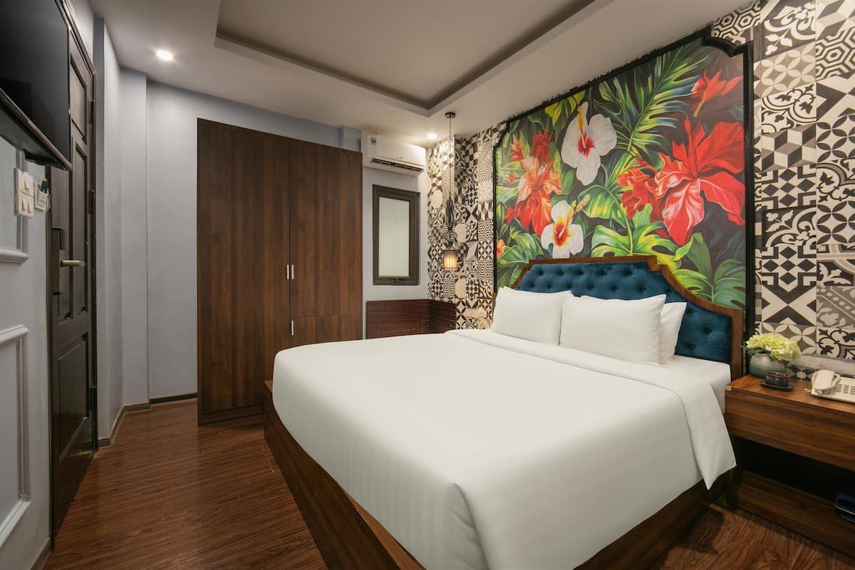 A hotel room with a large bed, a wardrobe, a mirror, and a floral-patterned wall.