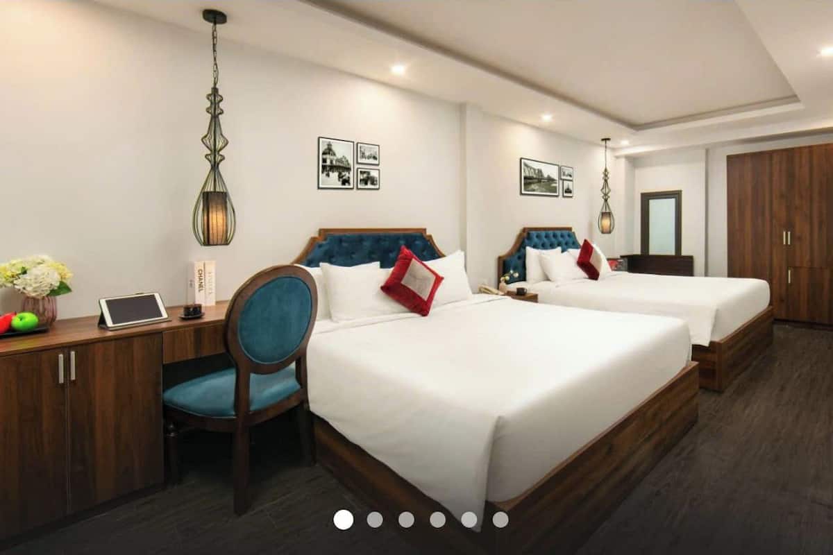 A hotel room with two beds, a desk with a laptop, a chair, and a desk lamp.