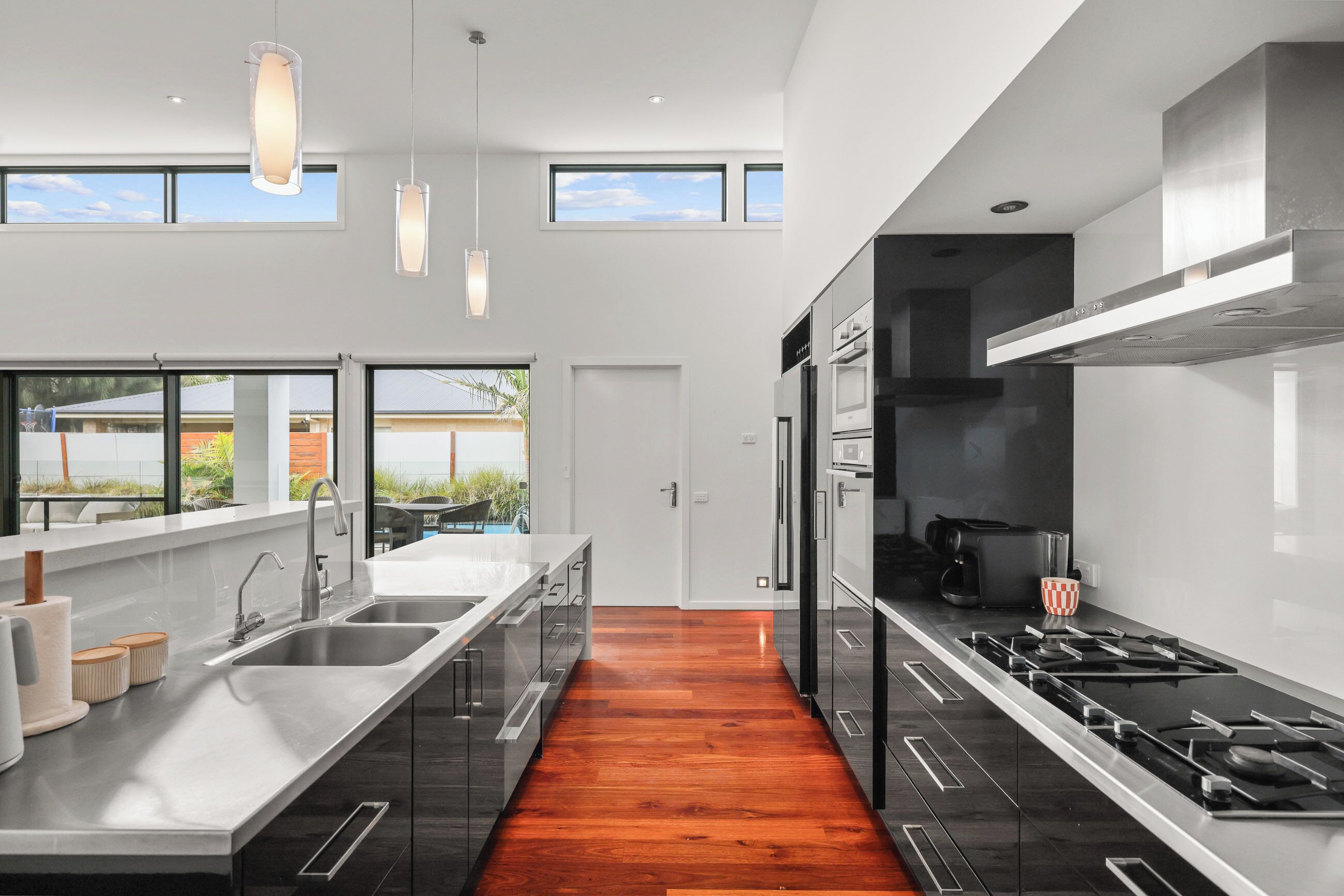 A modern kitchen with a central island, stainless steel appliances, and large windows offering views of the outdoors.