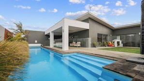 Une maison moderne dotée d’une piscine, d’un patio couvert et d’un espace de jeux avec des jouets.