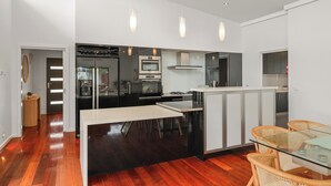 Une cuisine moderne dotée d’un îlot central, d’appareils électroménagers intégrés et de luminaires suspendus.