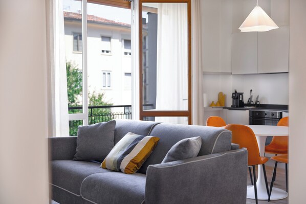 Una sala de estar moderna con un sofá gris, un cojín amarillo y azul a rayas, y sillones naranjas.