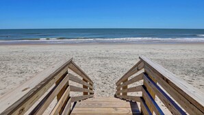 Une promenade en bois qui mène à une plage, avec un ciel bleu dégagé.