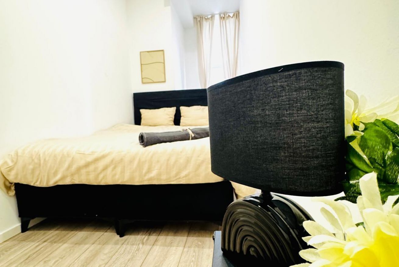 A bedroom with a bed, a dark-colored lamp, and a white flower.