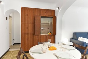 A dining area with a round table set for two, a wooden partition, and a blue sofa in the background. - Maisonette Apartment With Outdoor Dining (Genoa)