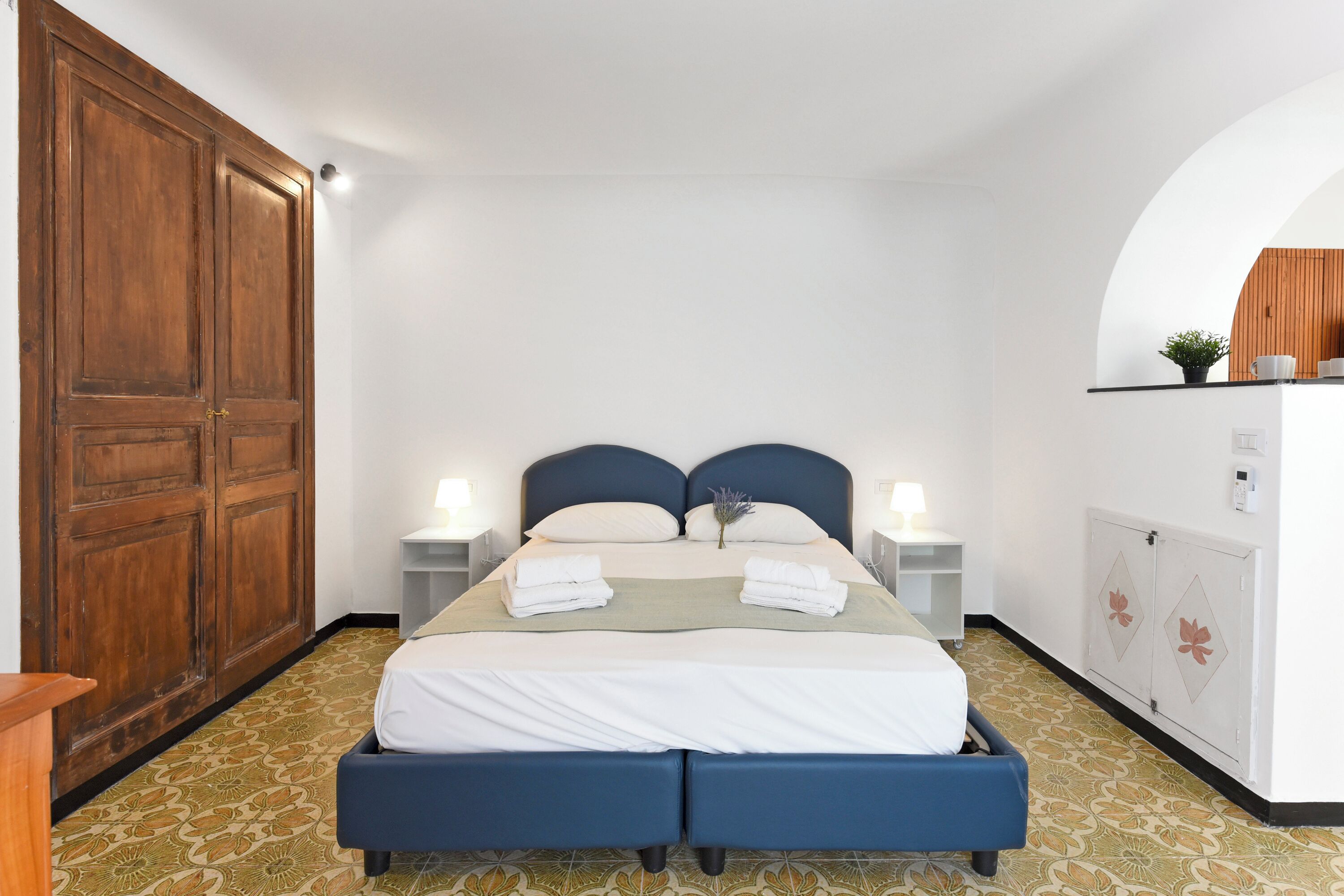 Une chambre d’hôtel avec un lit double, deux tables de chevet avec des lampes, une armoire et une petite plante en pot posée sur une étagère.