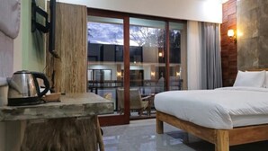Un dormitorio con una cama de madera, una mesita con un hervidor y vistas a un balcón con sillas.