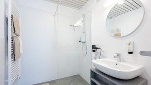 Une salle de bain moderne avec une douche à parois de verre, un lavabo blanc et un miroir rond.